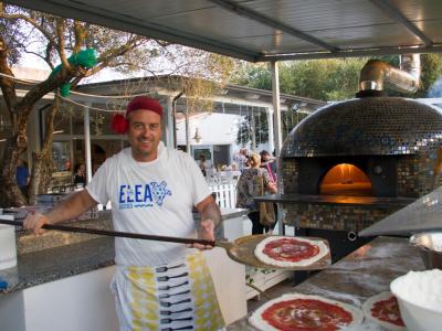 Pizzaiolo sorridente prepara pizze vicino a forno a legna.