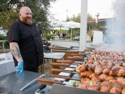 Chef avec barbecue extérieur, brochettes de viande grillées.