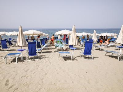 Plage avec chaises longues bleues et parasols blancs, vue sur mer.