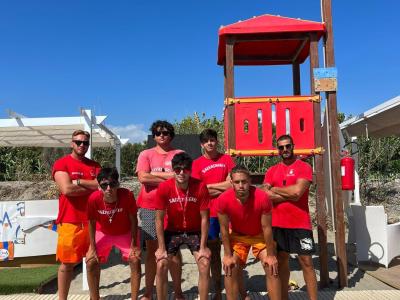 Bagnini in posa sulla spiaggia con torretta rossa.