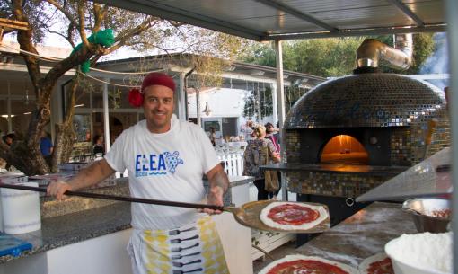 Pizzaiolo sorridente prepara pizze vicino a forno a legna.