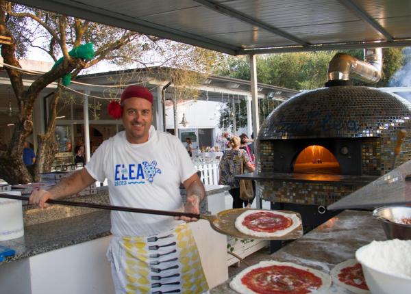 Pizzaiolo sorridente prepara pizze vicino a forno a legna.