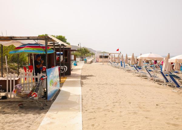 Plage de sable avec parasols, transats et kiosque.