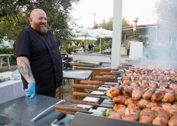 Chef avec barbecue extérieur, brochettes de viande grillées.