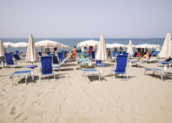 Plage avec chaises longues bleues et parasols blancs, vue sur mer.