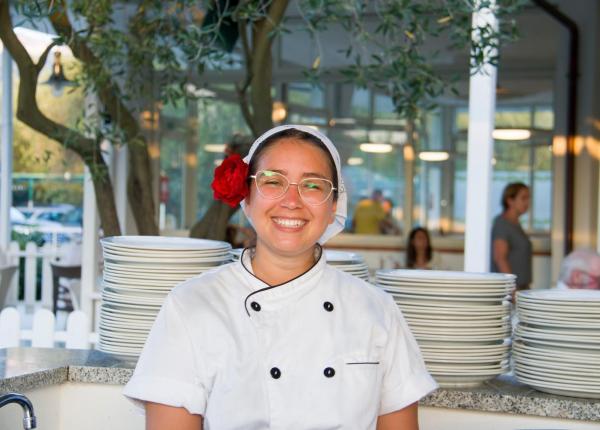 Chef souriante avec fleur rouge dans les cheveux, devant des assiettes empilées.