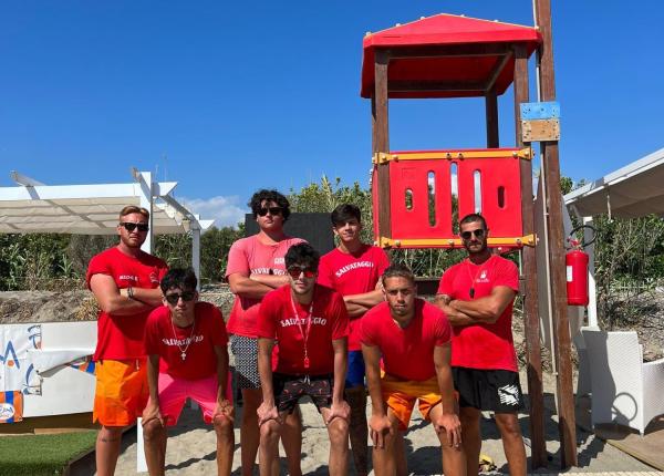 Bagnini in posa sulla spiaggia con torretta rossa.