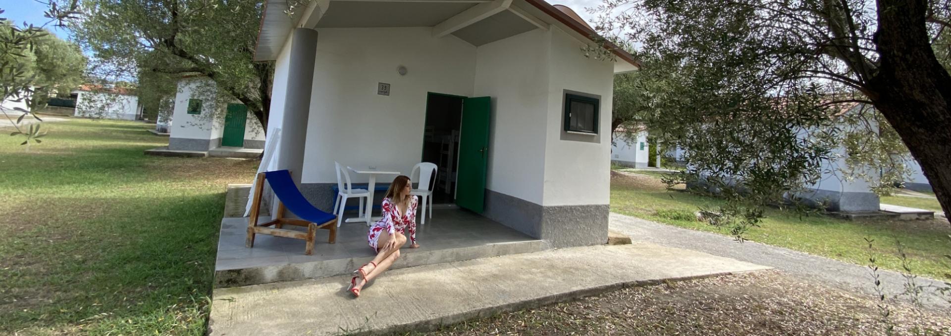 Donna seduta su veranda di bungalow bianco, circondata da alberi e prato verde.