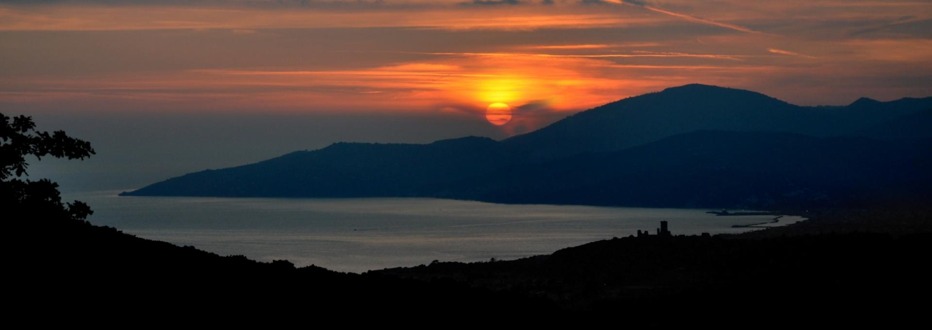 Tramonto sul mare con silhouette di montagne e cielo arancione.