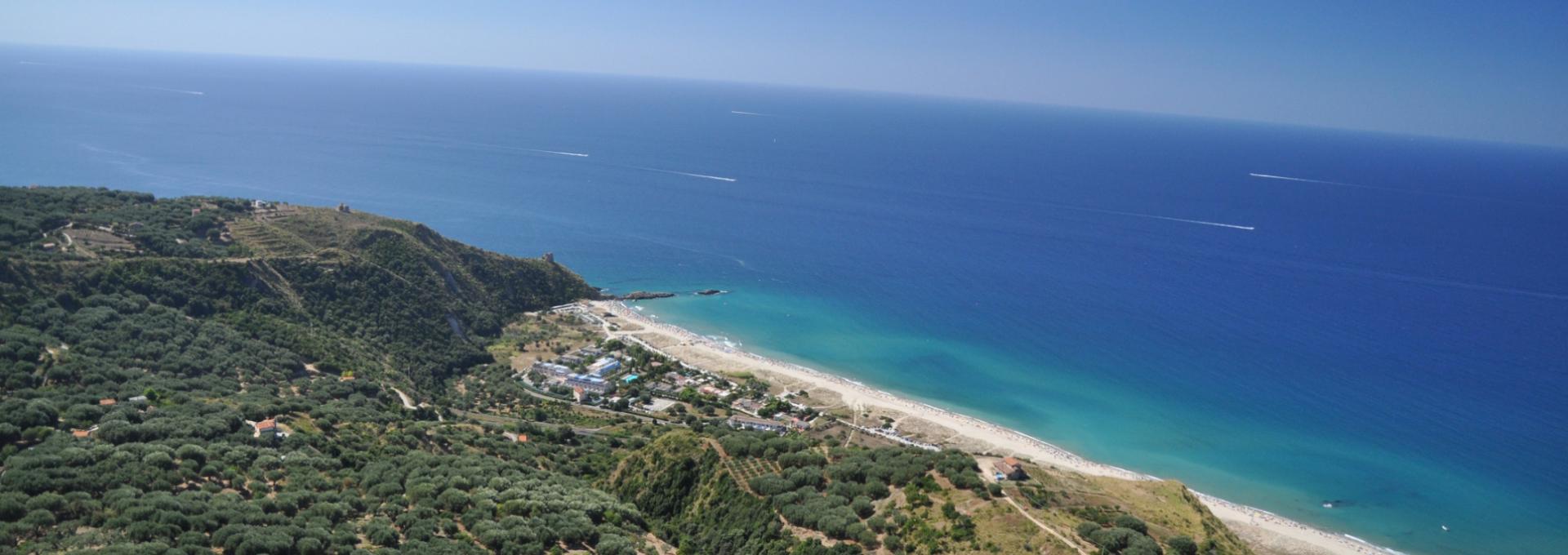 Vista aerea di una costa con mare blu e colline verdi.