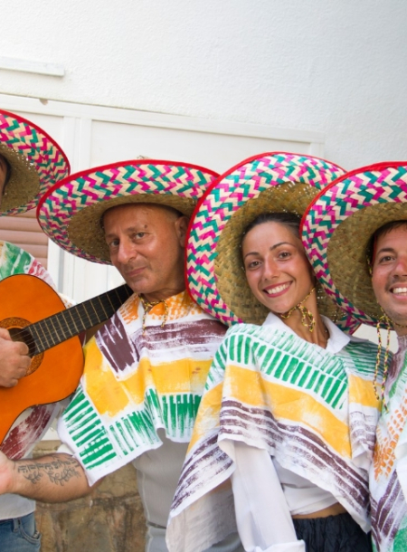 Gruppo di persone sorridenti con sombreri colorati e poncho, uno suona la chitarra.