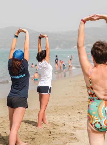 Persone fanno stretching sulla spiaggia in una giornata soleggiata.