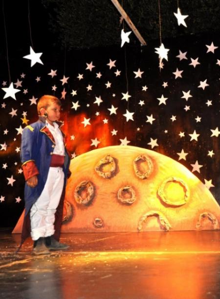 Bambino in costume su un palco stellato, con sfondo di luna e stelle.