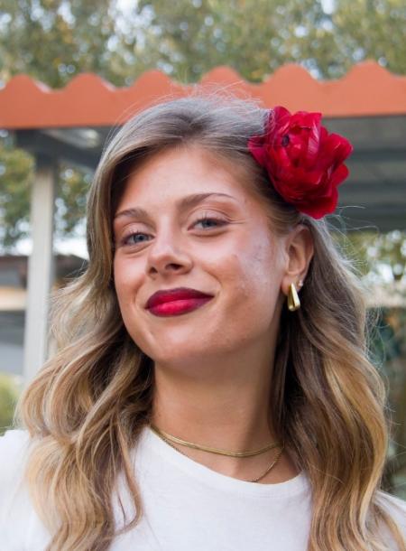 Donna sorridente con fiore rosso tra i capelli e rossetto abbinato.