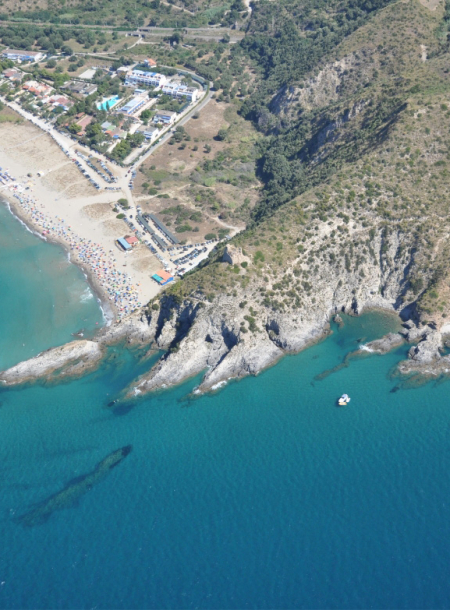 Spiaggia affollata con scogliere rocciose e mare cristallino, vista dall'alto.