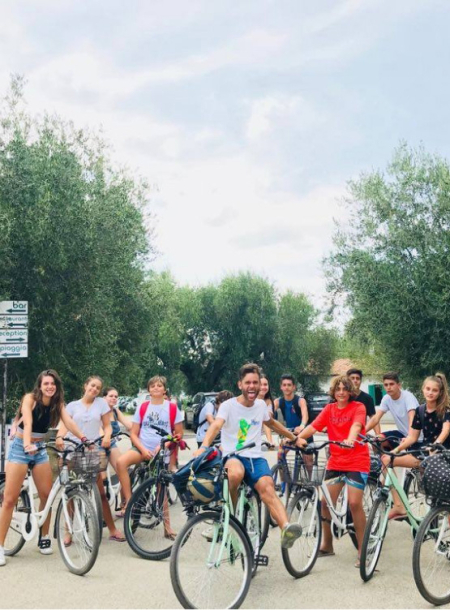 Gruppo di giovani in bicicletta su strada alberata, atmosfera di divertimento e amicizia.