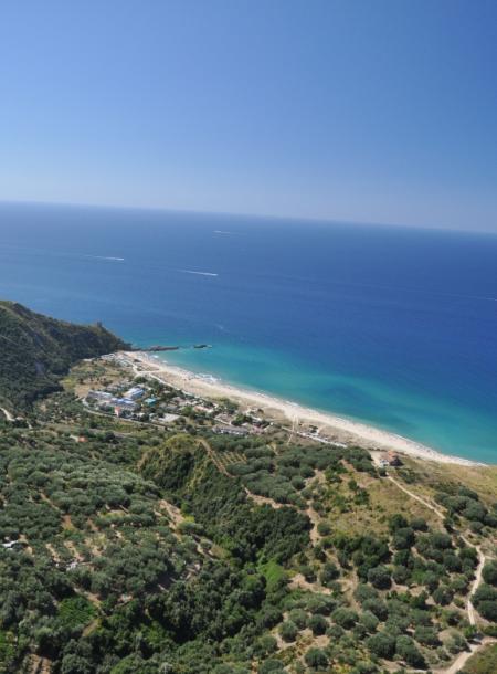 Vista aerea di una costa con mare azzurro e vegetazione verde.