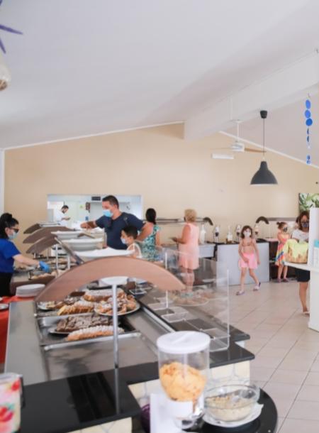 Persone servite al buffet, ambiente luminoso e spazioso, alcuni indossano mascherine.