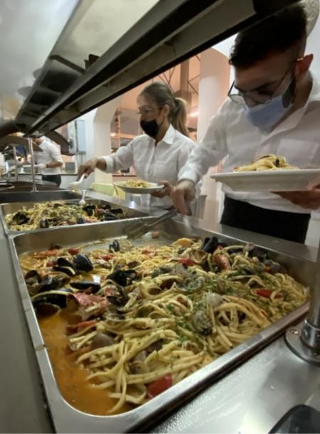 Buffet di pasta ai frutti di mare servito da personale in mascherina.