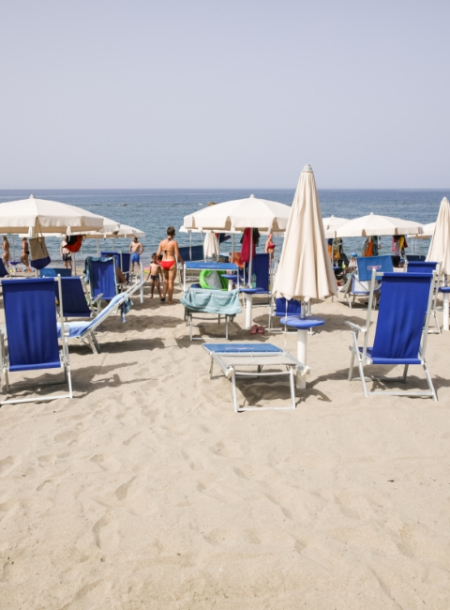 Spiaggia con ombrelloni bianchi e sdraio blu, persone godono del mare.