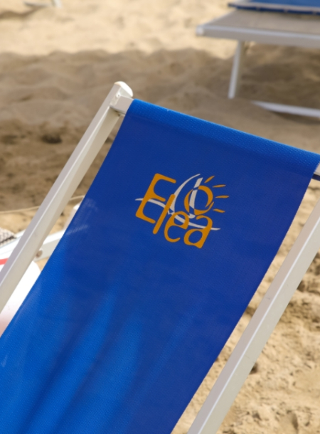 Sdraio blu sulla spiaggia con logo 'Elea' in giallo, sole stilizzato incluso.