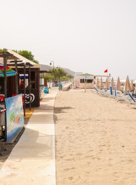 Spiaggia sabbiosa con ombrelloni chiusi e chiosco, bandiera rossa sventola.