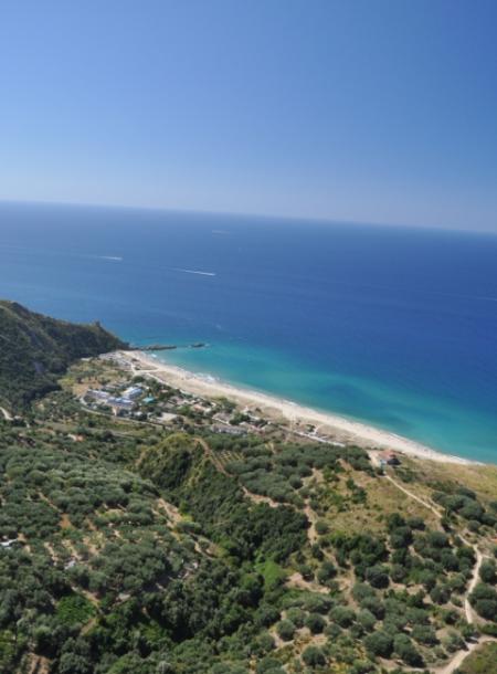 Vista aerea di una spiaggia con mare azzurro e colline verdi.