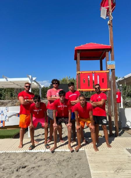 Gruppo di bagnini in posa davanti a una torretta sulla spiaggia.