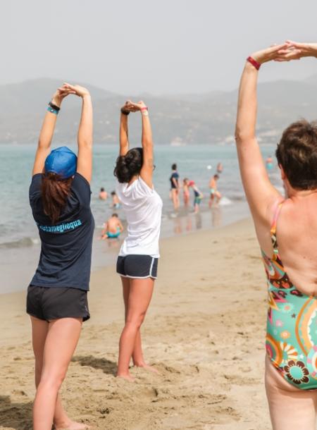 Persone fanno esercizi di stretching sulla spiaggia, con il mare sullo sfondo.