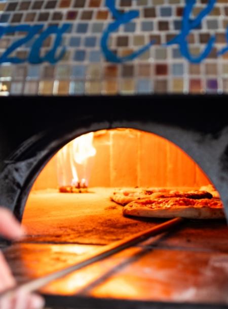 Pizza cuoce in un forno a legna con fiamme visibili.