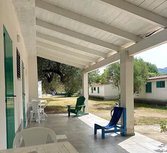 Veranda con sedie colorate, tavolo bianco e vista su giardino con alberi.