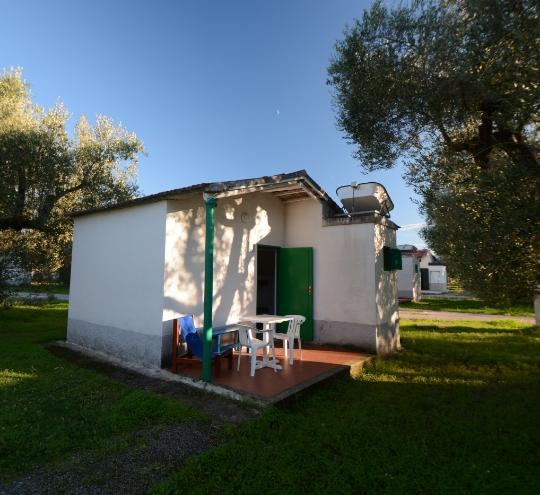 Piccola casetta bianca con veranda e tavolo esterno, immersa nel verde.