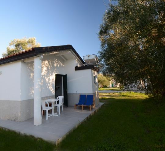 Piccola casa bianca con veranda, sedie e prato verde intorno.