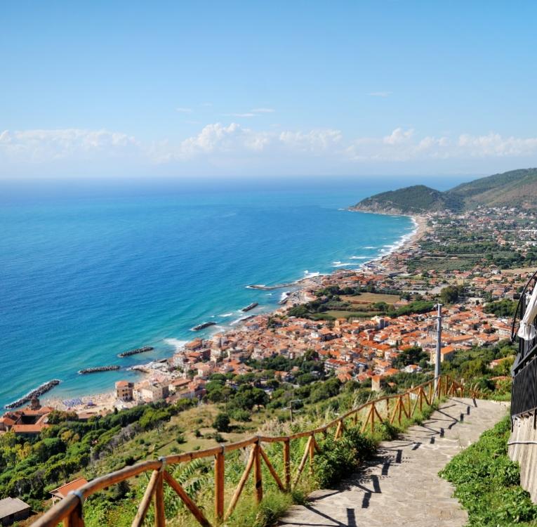 Vista panoramica di un borgo costiero con mare azzurro e colline verdi.