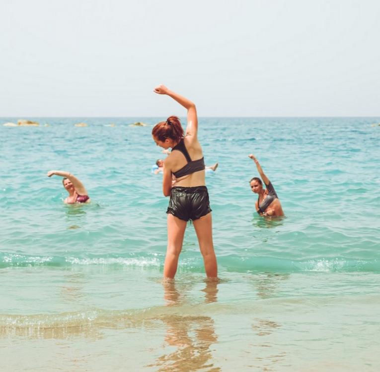 Persone fanno esercizi di stretching in acqua al mare sotto il sole.