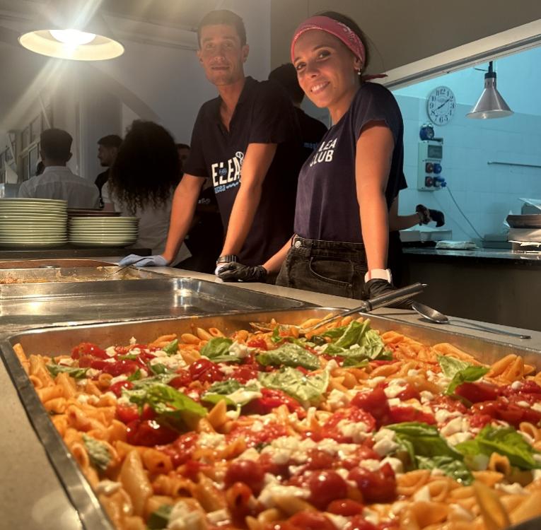 Due persone servono pasta al pomodoro e basilico in una cucina.