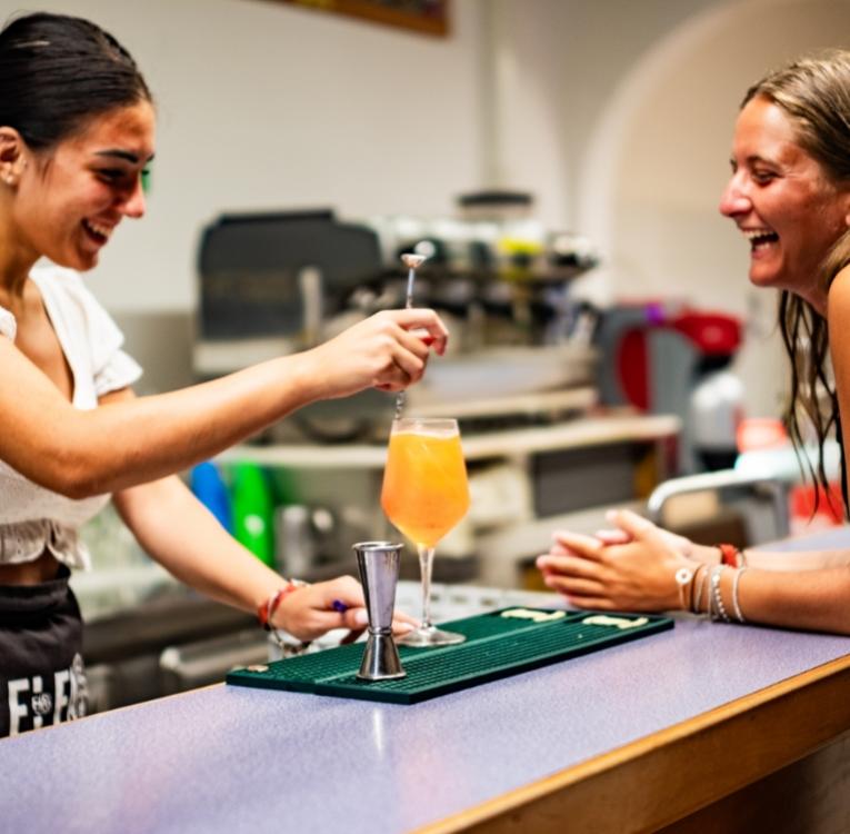 Due persone ridono mentre preparano un cocktail al bar.