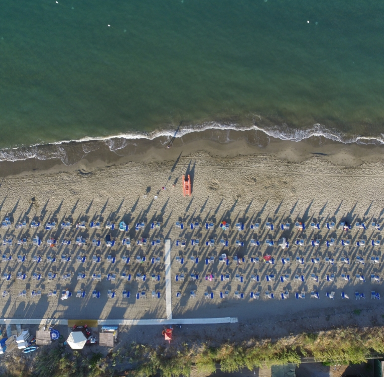 Spiaggia con ombrelloni e lettini allineati vista dall'alto, mare calmo.